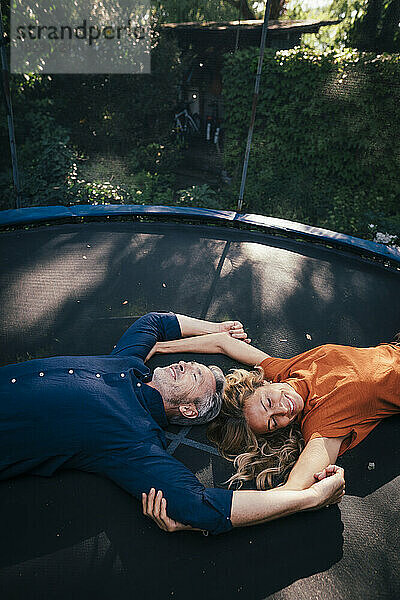 Happy mature couple lying on trampoline in back yard