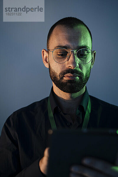 Geschäftsmann mit Brille hält Tablet-PC vor grauer Wand