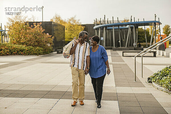 Glückliches älteres Paar hält sich an den Händen und geht auf dem Fußweg