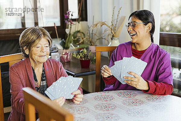 Glückliche Mitarbeiterin im Gesundheitswesen spielt mit einer älteren Frau zu Hause Karten