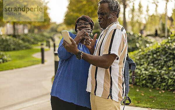 Ältere Frau lacht über Mann  der Smartphone im Park hält