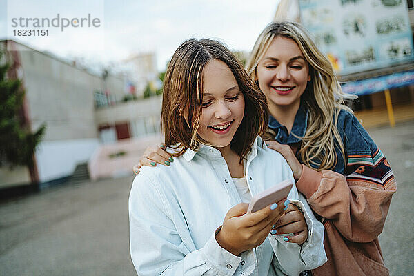 Lächelnde Mutter mit Tochter  die ihr Mobiltelefon benutzt