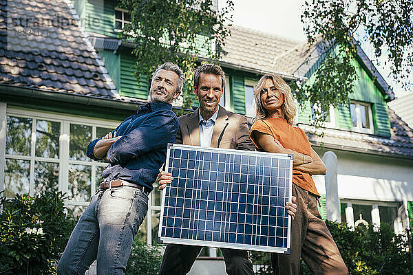 Selbstbewusster Mann und Frau mit Immobilienmakler  der Solarpanel durch Sonnenlicht auflädt