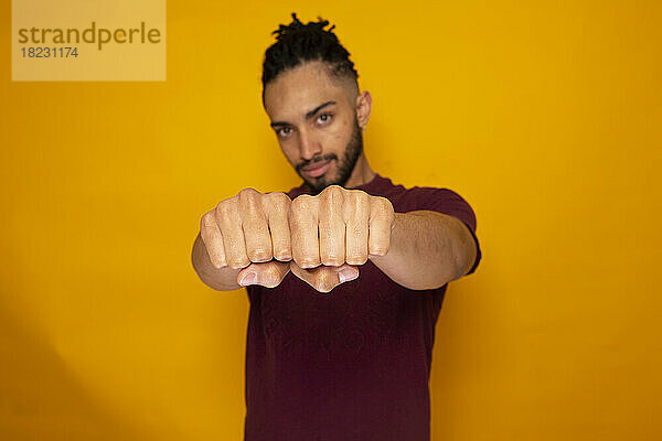 Confident man showing fists against yellow background
