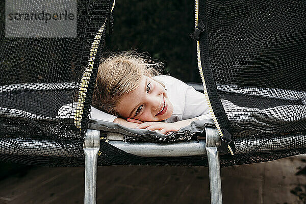 Lächelndes Mädchen liegt auf Trampolin im Garten