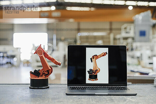 Laptop und Roboterarm auf dem Schreibtisch in der Industrie