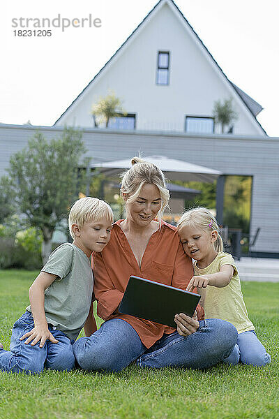 Glückliche Mutter teilt Tablet-PC mit Kindern im Garten