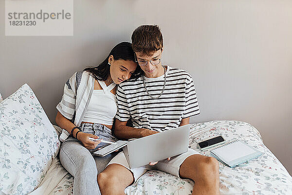 Mädchen lernt mit Bruder am Laptop im Schlafzimmer zu Hause