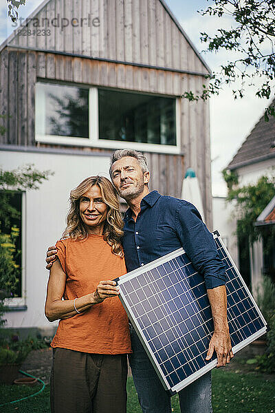 Lächelnde reife Frau mit Mann  der Solarpanel vor dem Haus hält