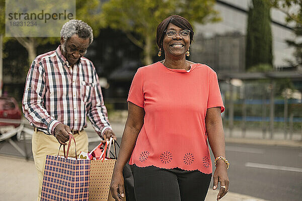 Lächelnde Frau geht mit Mann  der Einkaufstüten im Hintergrund hält