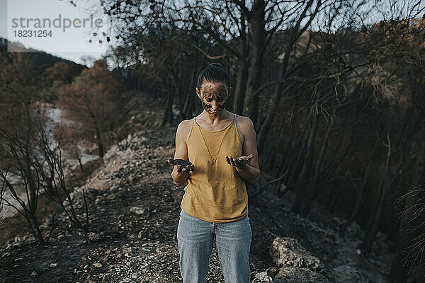 Frau blickt im Wald auf eine Hand voller Asche