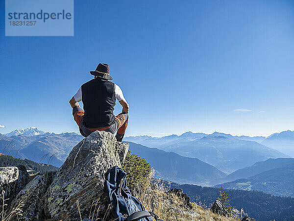 Älterer Mann mit Hut sitzt auf einem Felsen vor den Bergen im Nationalpark Vanoise  Frankreich