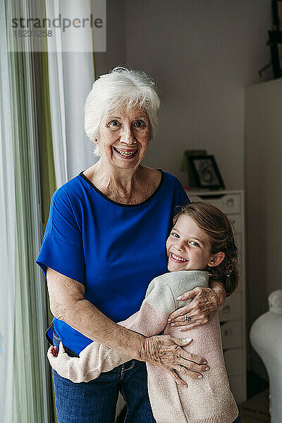 Glückliches Mädchen  das Großmutter zu Hause umarmt