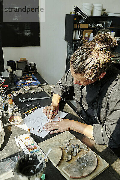 Handwerkerin skizziert Ringdesign auf Papier an der Werkbank
