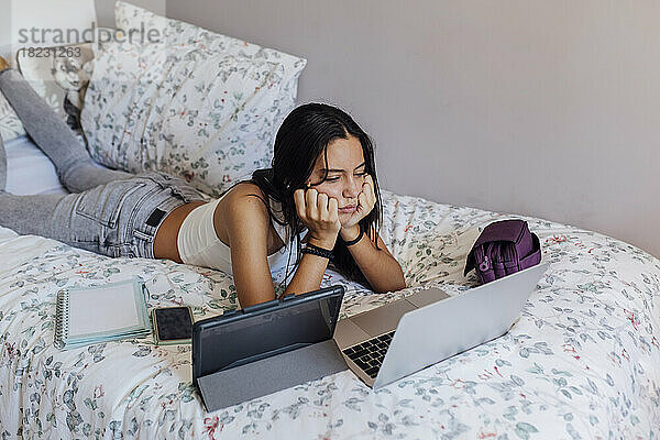 Mädchen mit Kopf in den Händen  das zu Hause im Bett auf den Laptop schaut