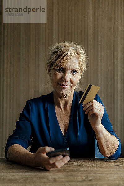 Lächelnde Geschäftsfrau mit Mobiltelefon und Kreditkarte im Büro
