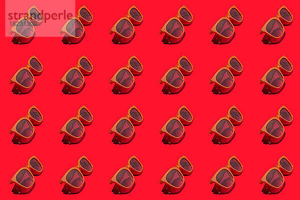 Muster aus Reihen von Sonnenbrillen im Retro-Stil  flach gelegt vor rotem Hintergrund