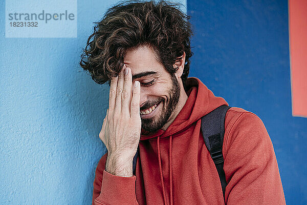 Happy man touching forehead by blue wall