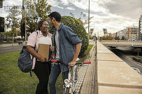 Junges Paar lacht und steht mit Fahrrad am Fußweg