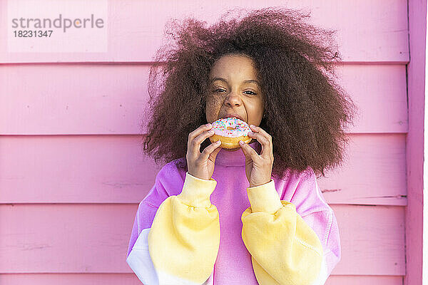 Hungriges Mädchen isst Donut vor rosa Wand