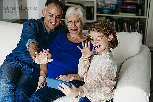 Glückliches Mädchen mit Großmutter und Vater  die zu Hause einen Videoanruf auf dem Mobiltelefon führen