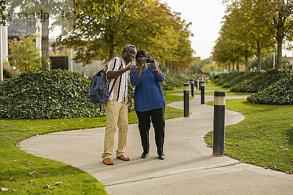 Frau fotografiert mit Kamera und steht neben Mann auf Fußweg im Park