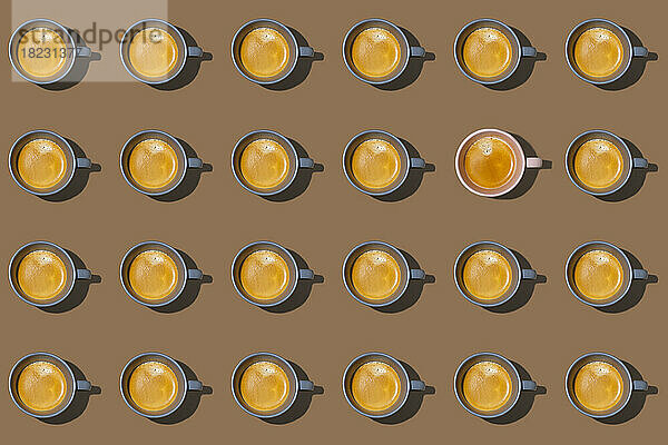 Muster aus in Reihen stehenden Kaffeetassen vor braunem Hintergrund  wobei eine einzelne anders aussieht