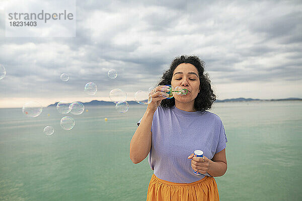 Frau bläst Seifenblasen vor dem Meer
