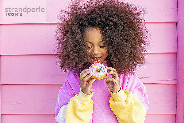 Afro-Mädchen isst Donut vor rosa Wand