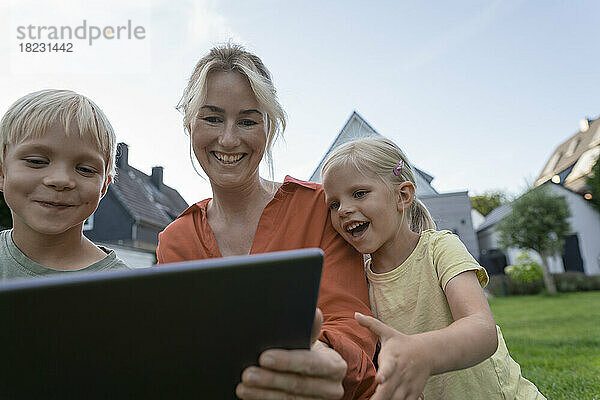 Glückliche Frau teilt Tablet-PC mit Kindern im Hinterhof