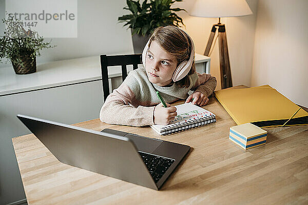 Mädchen sitzt mit Laptop und lernt zu Hause am Tisch