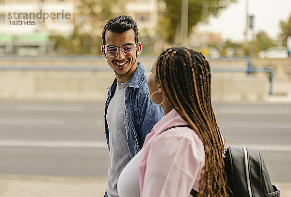 Lächelnder junger Mann geht mit Freundin am Fußweg spazieren