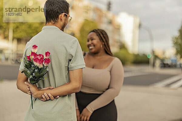 Junger Mann steht mit Blumenstrauß vor Frau am Fußweg