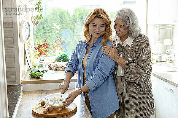 Ältere Frau und erwachsene Tochter bereiten in der Küche Teig für Brot zu