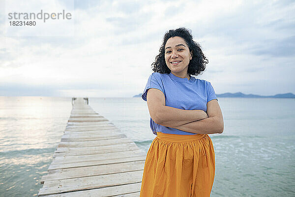 Happy woman standing with arms crossed on jetty
