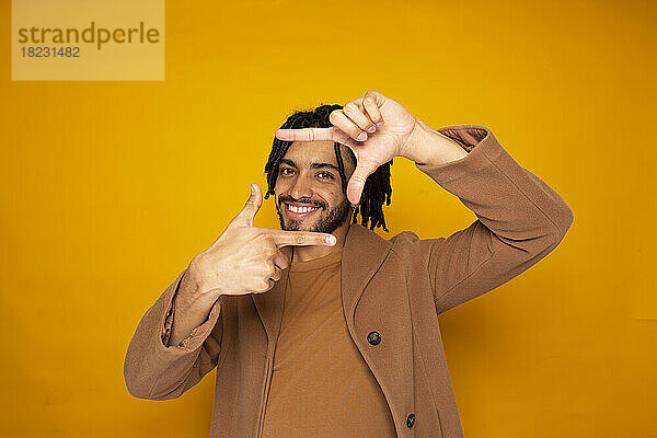 Smiling man making finger frame against yellow background