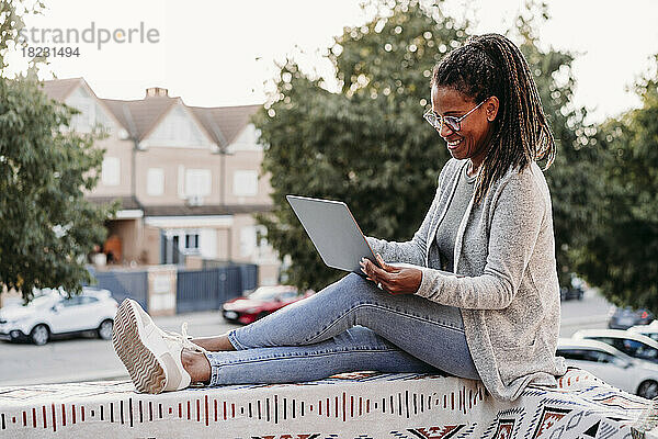 Glückliche Frau benutzt Laptop auf der Terrasse bei Sonnenuntergang