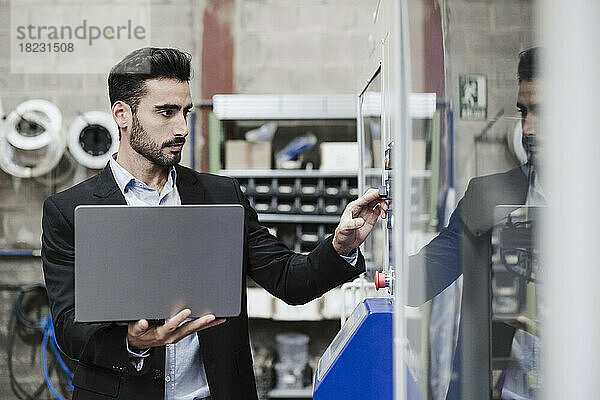 Ingenieur steht mit Laptop und bedient Maschinen in der Industrie