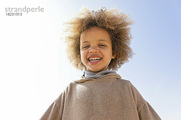Glückliches süßes Mädchen mit Afro-Frisur vor klarem Himmel