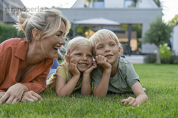 Glückliche Mutter blickt auf Kinder  die sich im Garten auf Ellbogen stützen