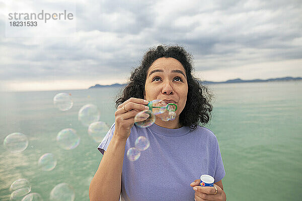 Woman enjoying blowing bubbles standing in front of sea