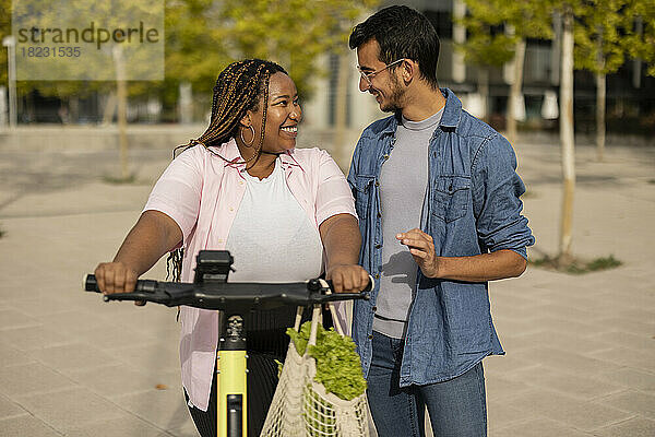 Glückliches Paar mit Elektroroller und Tüte Gemüse steht am Fußweg