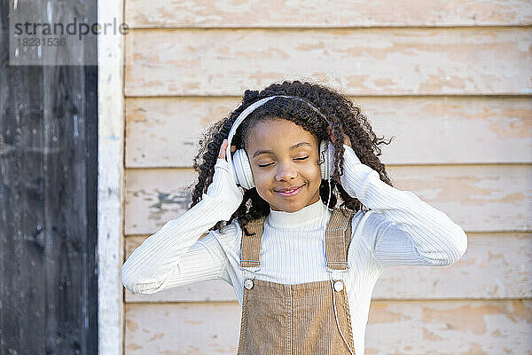 Lächelndes Mädchen  das über Kopfhörer vor der Wand Musik hört
