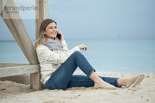 Lächelnde schöne junge Frau  die am Strand mit ihrem Smartphone spricht