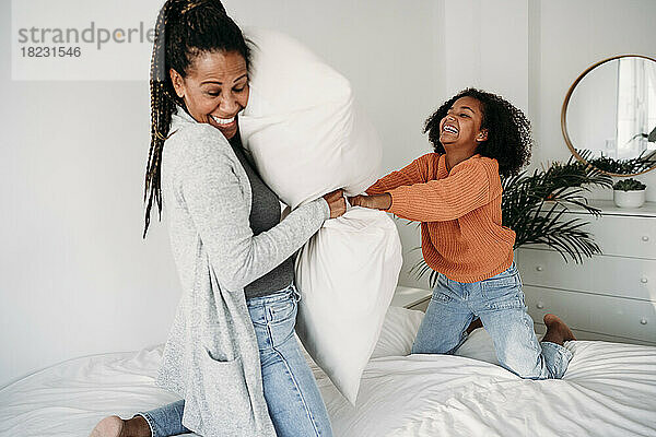 Fröhliche Mutter und Tochter spielen zu Hause mit Kissen im Bett