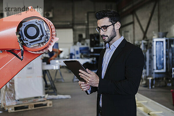 Ingenieur nutzt Tablet-PC und steht neben Roboterarm in der Industrie