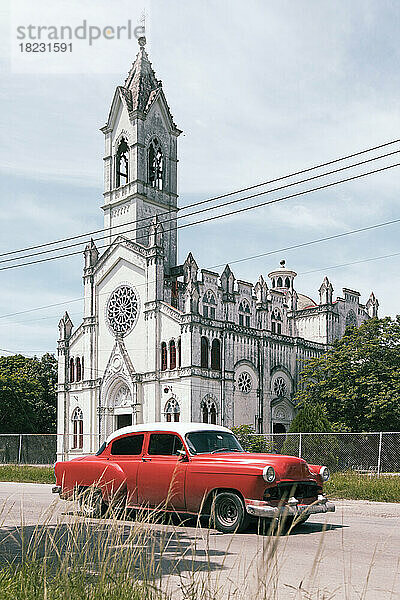 Kuba  Havanna  roter Oldtimer parkt vor einer weiß gestrichenen Kirche im Viertel La Vibora