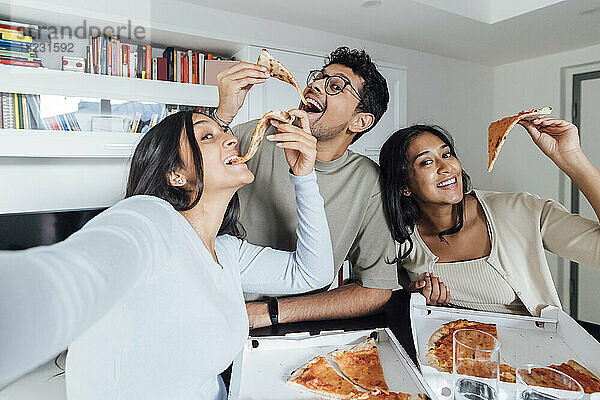 Glückliche junge Frau macht ein Selfie mit Frau und Mann  die zu Hause Pizza essen