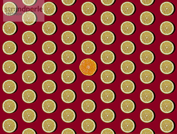 Pattern of halved lemons flat laid against red background with single tangerine in center
