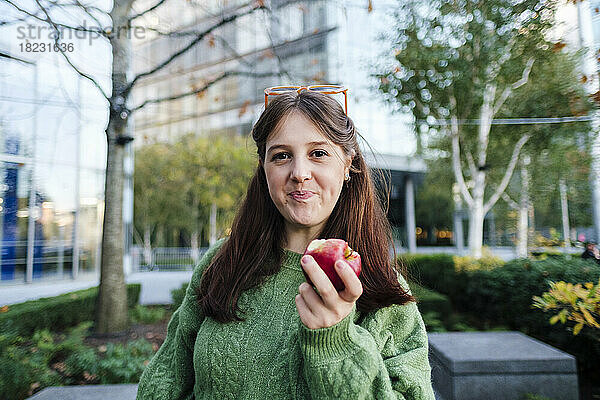 Lächelnde Frau hält Apfel vor Gebäude